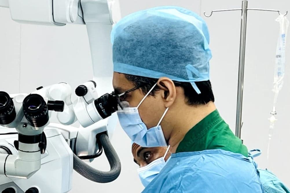 Dr. Adnan in surgical scrubs operating with a surgical microscope